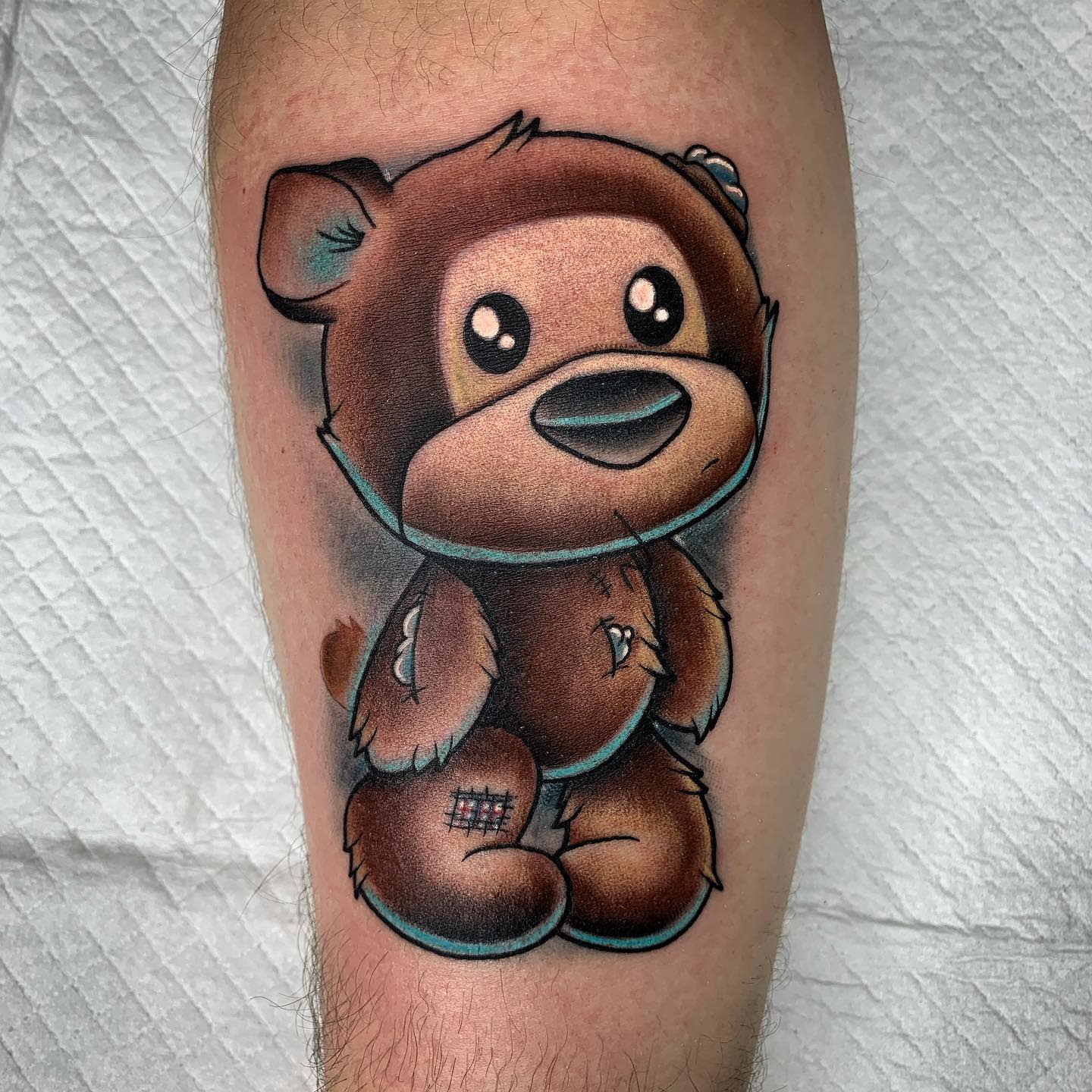 Tattoo of a cute, worn-out teddy bear with patches and stitches on an arm